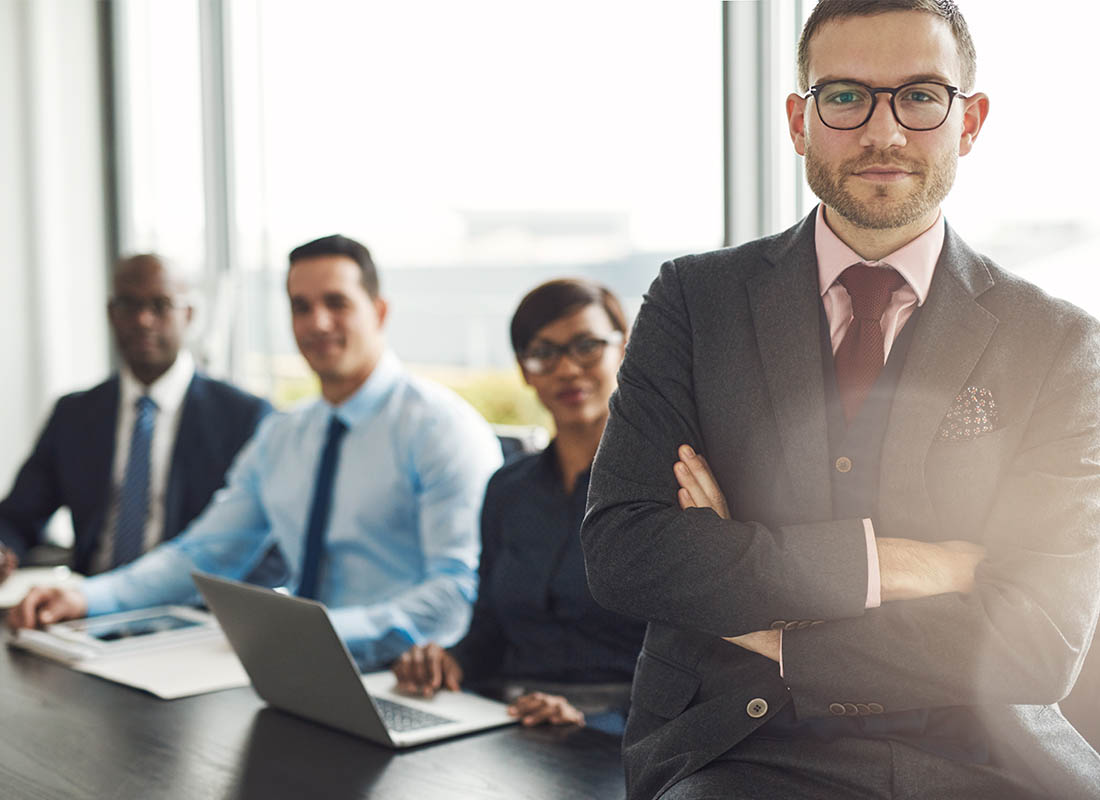 Meet Our Team - Professional and Welcoming Group at a Conference Table Faces the Camera, Team Leader Sitting on the Table with Arms Folded